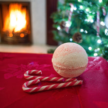 Load image into Gallery viewer, Candy Cane bath bomb pictured with Candy canes & with a fireplace & christmas tree background